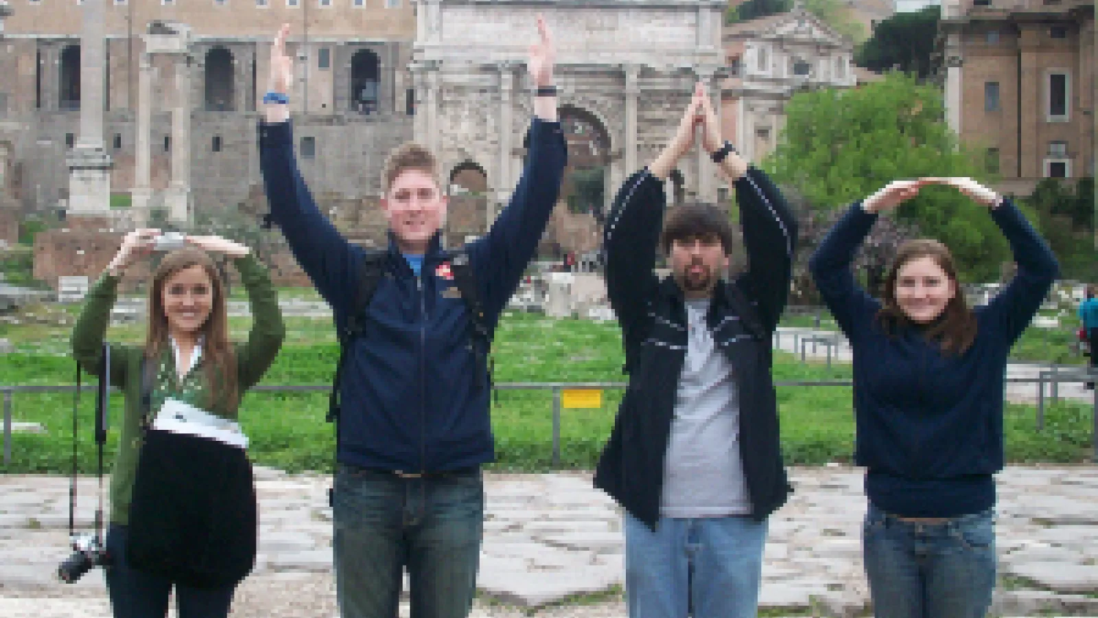 Students make an Ohio State symbol with their arms in front of Roman ruins.