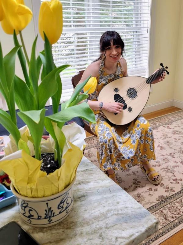 A photo of Ari in a yellow dress, playing the oud