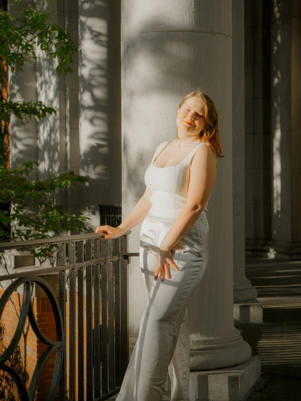 Rachel Gastrich, wearing white pants and a white top, leaning against a column